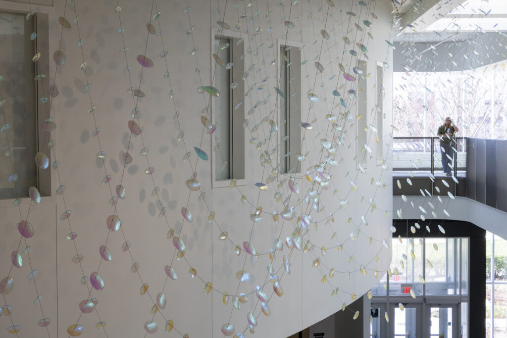 Detail view of suspended glass petals and leaves-- Glass suspended sculpture composed of 2,000 dichroic glass flower petals and leaves, suspended from a 30-foot ceiling. Installed inside Steven Wymer Hall, University of Illinois Urbana-Champaign.