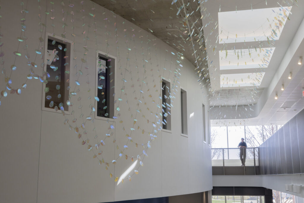 Direct sunlight streaming from skylight above -Glass suspended sculpture with 2,000 dichroic glass flower petals and leaves inside Steven Wymer Hall, University of Illinois Urbana-Champaign