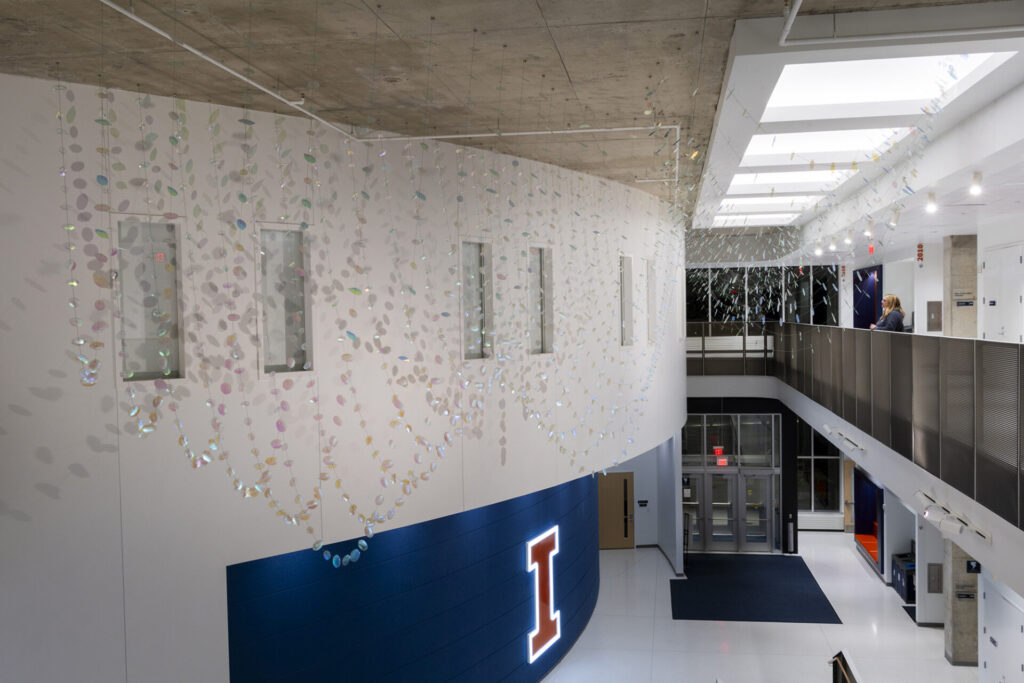 Night time view of Glass suspended sculpture with 2,000 dichroic glass flower petals and leaves inside Steven Wymer Hall, University of Illinois Urbana-Champaign